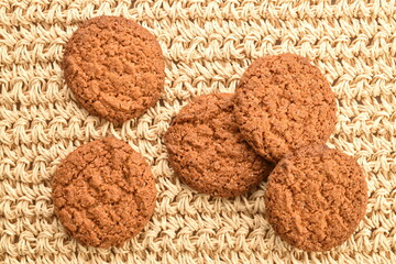 Several dark brown oatmeal cookies on a straw mat, close-up, top view.