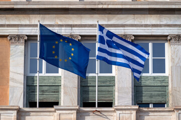 Athens, Attica, Greece. European Union's and Greece's flags waving in front of the greek parliament neoclassical building. Sunny day