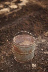 Old tall bucket with sand stands in a vegetable garden on damp s
