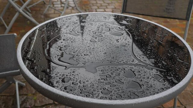 Romantic woman draw heart shape on wet glass of small table, close shot of round top. Street terrace of small cafe empty at rainy weather, old buildings reflection on surface