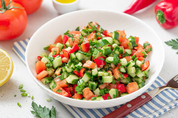 Vegetable salad in a white plate on a light background. Salad with tomatoes, cucumbers, peppers, parsley and lemon. Vegan or diet food.