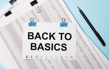 A sheet of paper with the text BACK TO BASICS lies on the documents near the pen on a light blue background. Business concept
