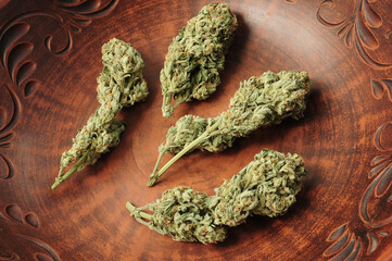 Cannabis buds in brown clay dish, flat lat, top view. Marijuana flowers close-up. Hemp recreation,...