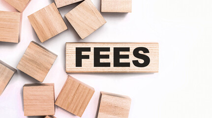 On a light background, wooden cubes and a wooden block with the text FEES. View from above
