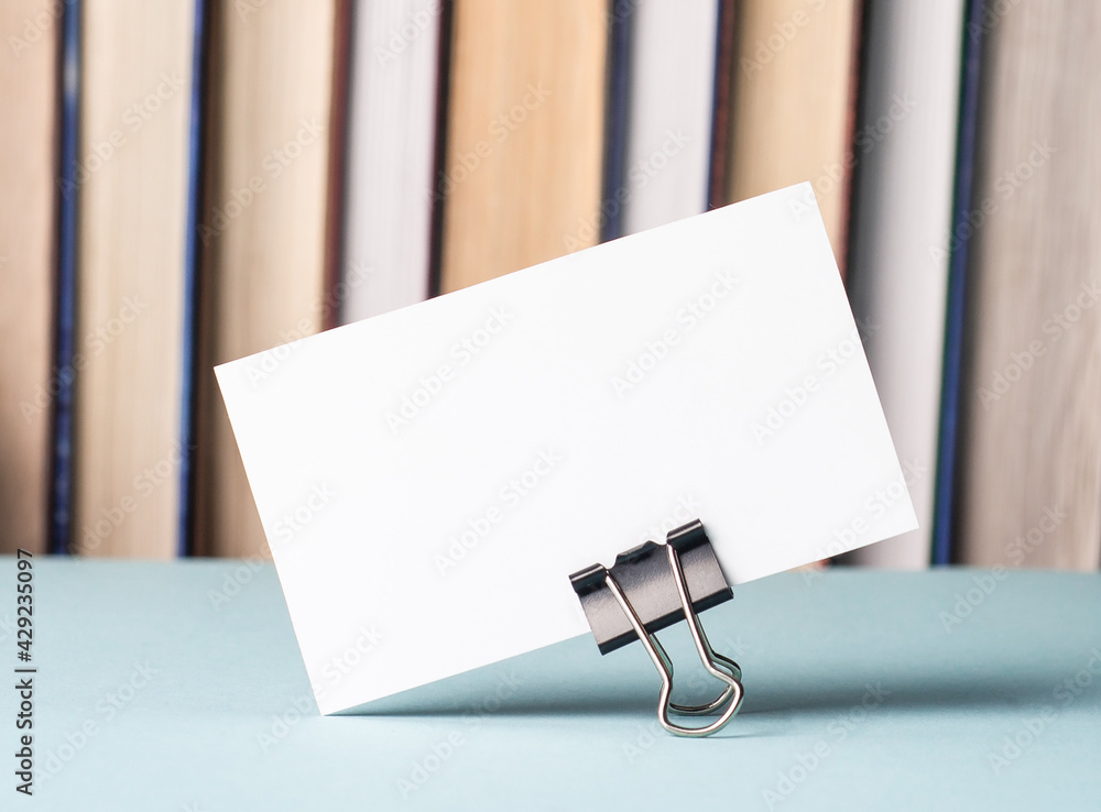 Poster there is a white blank card with a place to insert text on the table against the background of books