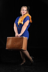 Fat woman dressed in the style of the 20-30s of the last century with a suitcase on a dark...