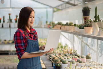 A beautiful Asian woman in a red and blue scottish shirt stands. holding a laptop On the farm cactus to accept orders for a cactus from an online market customer