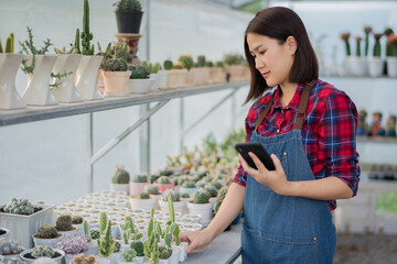 A beautiful Asian woman in a red and blue scottish shirt  Are using smartphones in Cactus Farm to get Cactus orders from customers in online market.