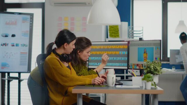 Confident women photo editors sitting at workplace in creative studio retouching photo, art director explaning color greding technic. Retouchers editing with drawing tablet and stylus pencil