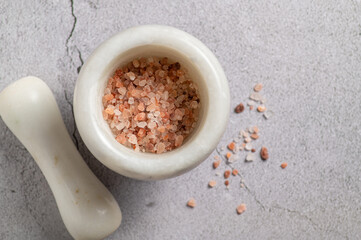 Large pink himalayan salt in a mortar for seasoning on a marble background, top view