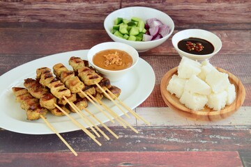 Indonesian chicken satay or Sate Ayam  with lontong. Served with sweet soy sauce, peanut sauce and pickles cucumber and onion