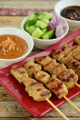 Indonesian chicken satay or Sate Ayam. Served with sweet soy sauce, peanut sauce and pickles cucumber and onion
