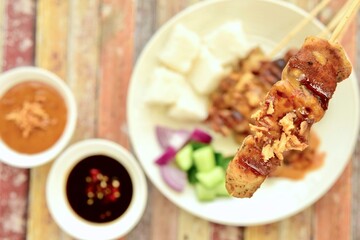 Indonesian chicken satay or Sate Ayam  with lontong. Served with sweet soy sauce, peanut sauce and pickles cucumber and onion