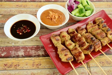 Indonesian chicken satay or Sate Ayam. Served with sweet soy sauce, peanut sauce and pickles cucumber and onion