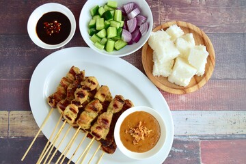 Indonesian chicken satay or Sate Ayam  with lontong. Served with sweet soy sauce, peanut sauce and pickles cucumber and onion