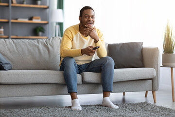 Happy black man watching TV at home, copy space