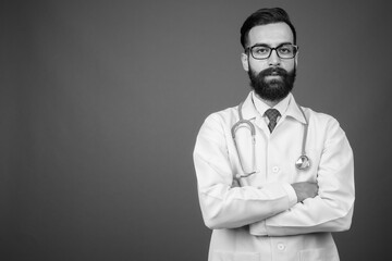 Young handsome bearded Persian man doctor against gray background