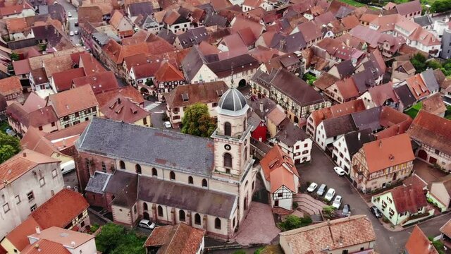Old church building at Saint-Hippolyte town, aerial orbiting shot, camera fly around tower and zoom in. Landmark in middle of beautiful Alsatian village, half timbered houses seen around.