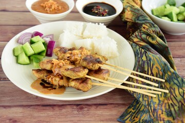 Indonesian chicken satay or Sate Ayam  with lontong. Served with sweet soy sauce, peanut sauce and pickles cucumber and onion
