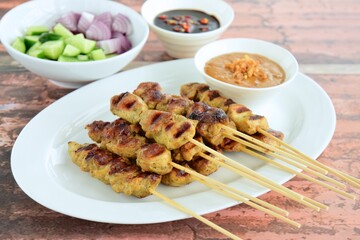 Indonesian chicken satay or Sate Ayam. Served with sweet soy sauce, peanut sauce and pickles cucumber and onion