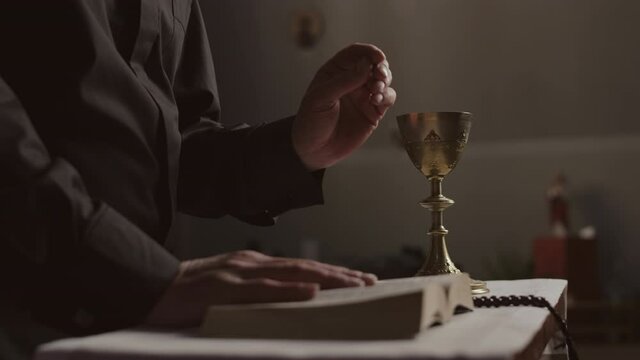 Medium shot of unrecognizable pastor wearing black robe standing at altar and preaching sermon in Christian church during Eucharistic rite