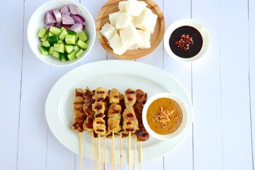 Indonesian chicken satay or Sate Ayam  with lontong. Served with sweet soy sauce, peanut sauce and pickles cucumber and onion