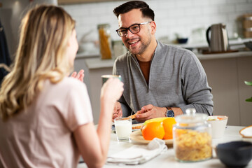 Beautiful man enjoying in breakfast with his girffriend. Happy young couple drinking coffee and eating sandwich at home.