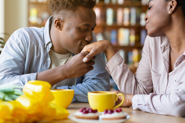 Romantic young man kissing his beloved woman's hand on festive Valentine's dinner at cozy cafe