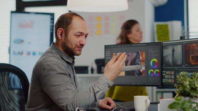 Video editor talking on videocall holding smartphone editing movie sitting in start up creative agency. Videographer processing film montage in digital multimedia company with post production software