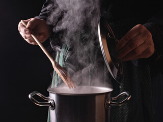The cook is in the kitchen. Close-up of an open saucepan lid and a chef's hand with a wooden fork...