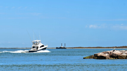 Broadside view of a beautiful white and black fishing yacht boat sails past rock breakwater on the calm blue water on a sunny day.