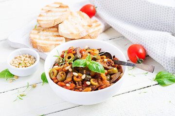 Traditional Italian Caponata and toast on a wooden white table. Sicilian caponata.