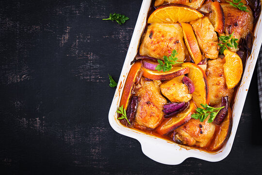 Baked chicken thighs. Appetizing slices of baked chicken with red onion and oranges in a baking dish. Top view, copy space