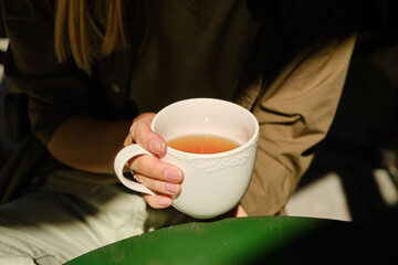 A woman with a cup of hot tea in her hands sits on the summer terrace of the restaurant. The girl drinks aromatic tea in a cozy morning. Enjoy the moment, take a break. Quiet freelance lifestyle