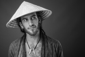Young handsome Hispanic man with dreadlocks wearing Asian conical hat in black and white