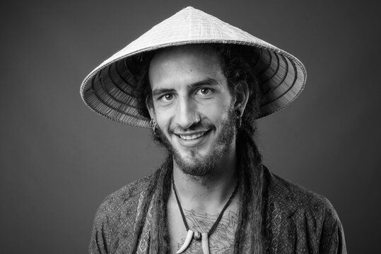 Young Handsome Hispanic Man With Dreadlocks Wearing Asian Conical Hat In Black And White