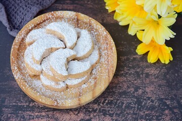 Fototapeta na wymiar Putri Salju or crescent-shaped cookies coated with powdered sugar. Traditional Indonesian cookies to celebrate Eid al Fitr. Decorated with yellow flower on wooden background