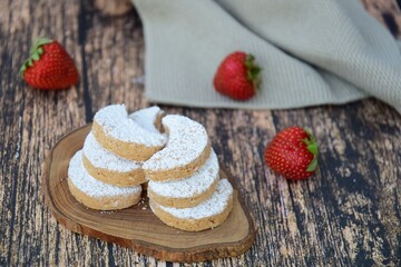 Putri Salju or crescent-shaped cookies coated with powdered sugar. Traditional Indonesian cookies to celebrate Eid al Fitr. Decorated with strawberries on wooden background
