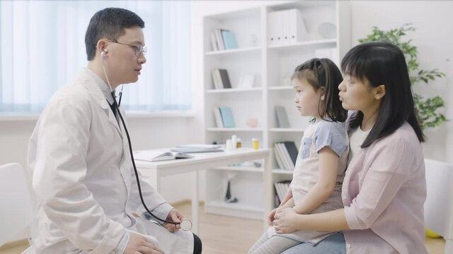 Pediatrician examining asian girl mother and child visiting doctor for treatment