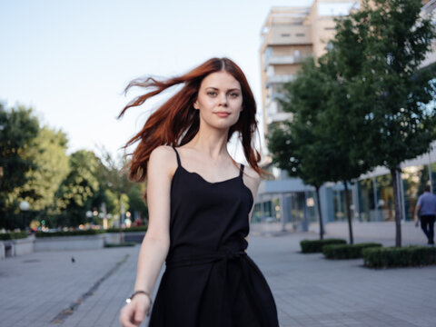 Fashionable Woman in a black dress walks down the street in the park in nature