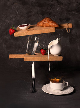 Breakfast concept. Croissant, cup of coffee, cream, milk, strawberries. Food on wooden cutting boards, levitation. Splashes. Black background