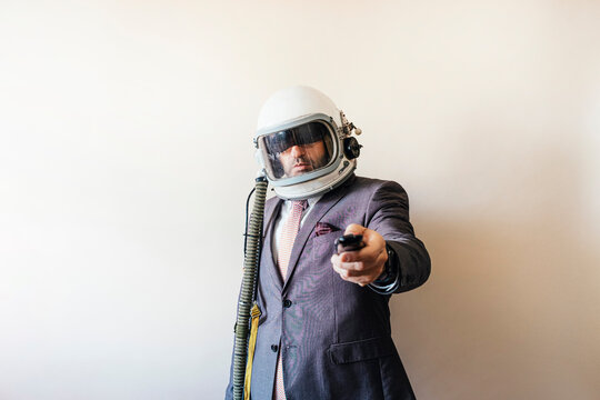 Businessman with astronaut helmet using a television remote control
