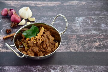 Beef Rendang, spicy beef stew from Indonesia. Served in a wok on wooden background