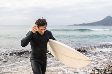 Obraz premium Happy surfer getting out of the water after surfing with smiling face