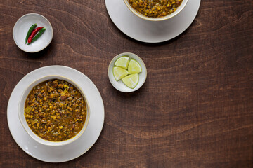 Two whole mung bean curry plates with limes and chili on wooden table. Flat lay, top view.