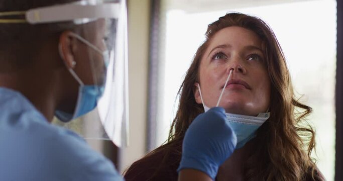 African american female doctor wearing face mask giving covid swab test to female patient