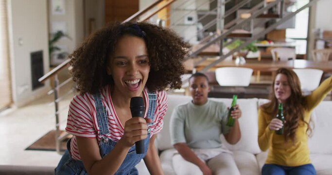 Diverse group of female friends having fun singing karaoke and drinking beer at home