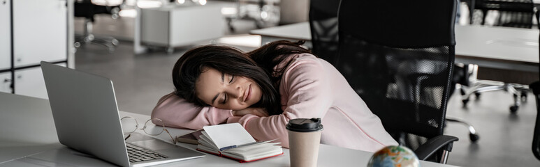 tired student sleeping on desk near laptop and paper cup, banner