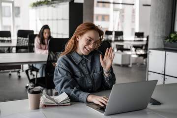 cheerful redhead student waving hand while having video chat on laptop