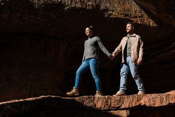 a couple walks hand in hand through a rocky landscape, the girl leading the boy.